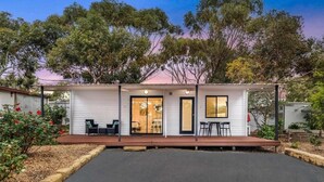 Een modern, gelijkvloers huis met een overdekt terras, grote ramen en uitzicht op omliggende bomen.