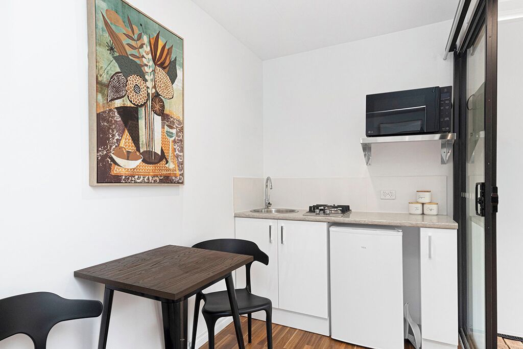A compact kitchen with white cabinets, a microwave, a sink, and a dining table with two chairs.