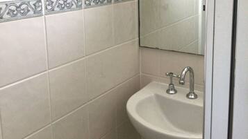 A bathroom with white tiles, a sink, and a mirror.