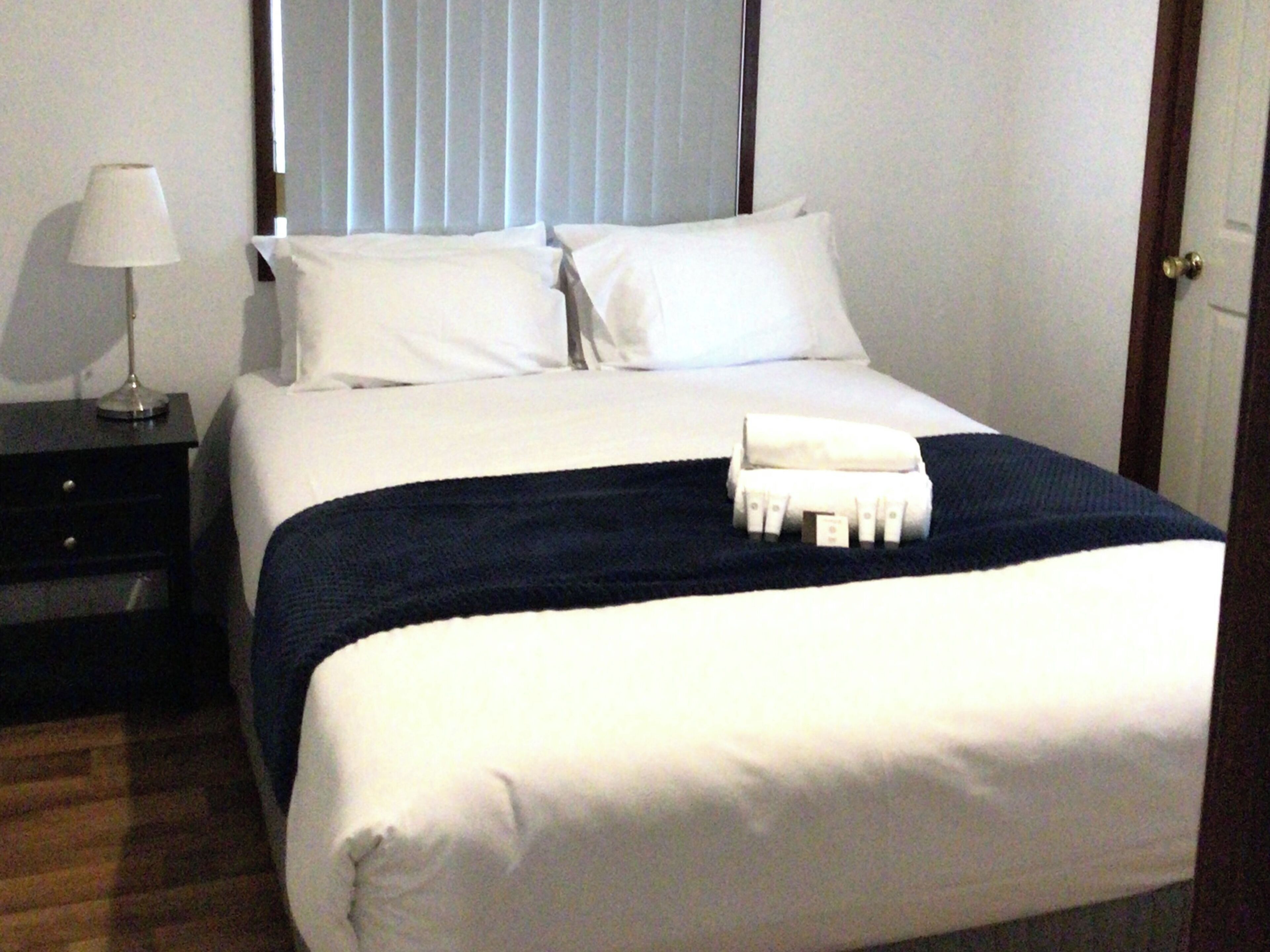 A neatly made bed with white linens, a dark blue throw blanket, and a folded white towel on the bed.