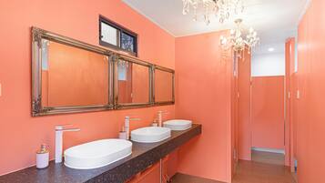 Un baño con tres lavabos, un espejo grande y una araña.
