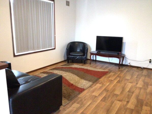 A living room with a black leather sofa, a television on a wooden stand, and a patterned rug on a wooden floor. - Northam Holiday Park (Northam)