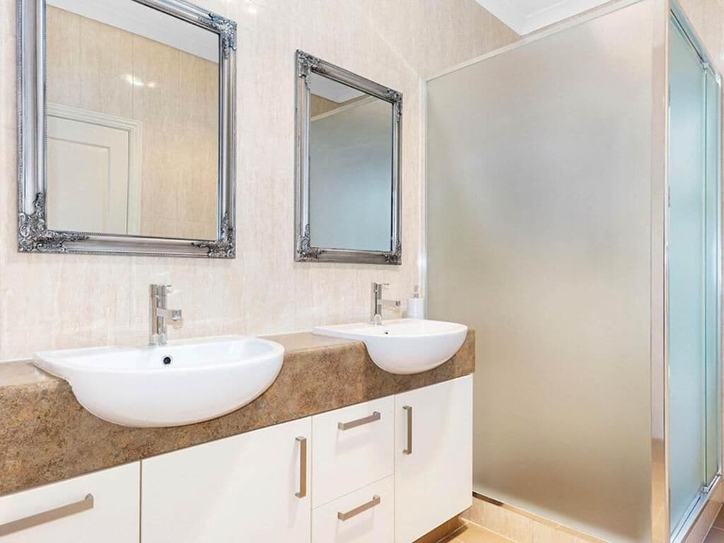 A bathroom with two sinks, two mirrors, and a glass shower door.