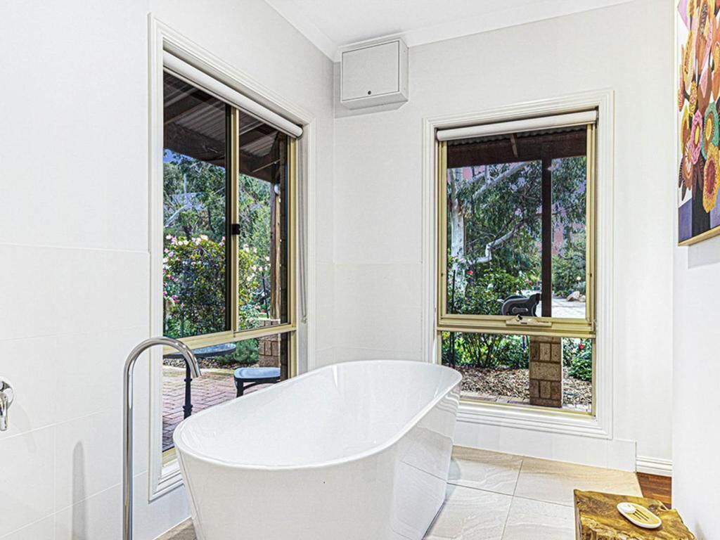 Un baño moderno con una bañera independiente, ventanas amplias y vistas a zonas verdes al exterior.