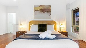 Een hotelkamer met een groot bed, twee nachtkastjes met lampen, een schilderij boven het bed, en een raam aan de rechterkant.