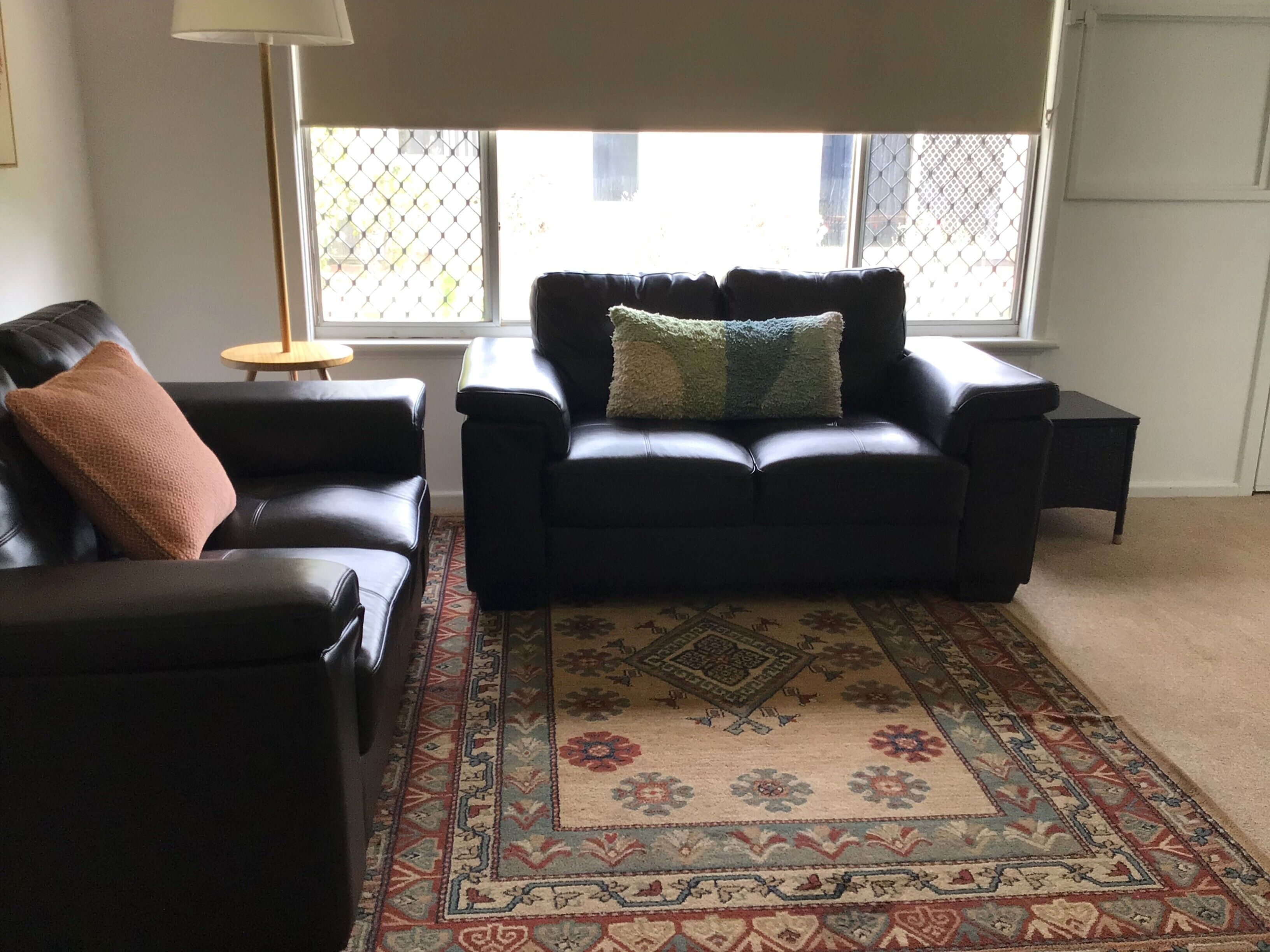 A living room with a black leather sofa, a matching armchair, and a patterned rug.