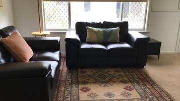 A living room with a black leather sofa, a matching armchair, and a patterned rug.