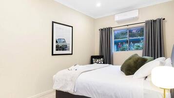 A bedroom with a bed, a window with curtains, a framed picture on the wall, and an air conditioning unit.