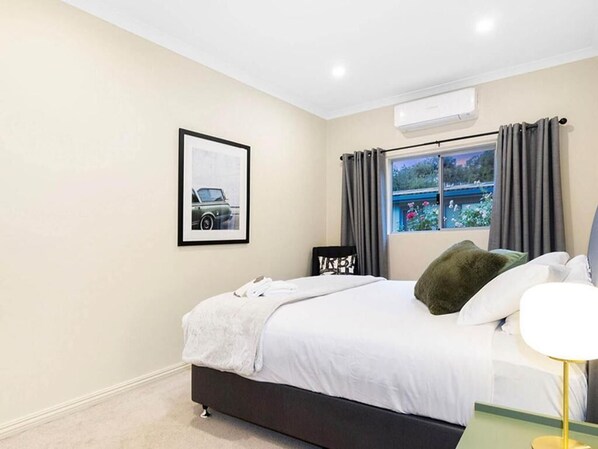 Un dormitorio con cama, ventana con cortinas, un cuadro en la pared y un equipo de aire acondicionado.