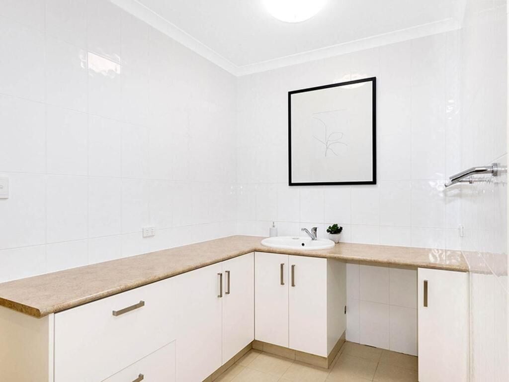 A bathroom with white tiles, a beige countertop, and a framed artwork on the wall.