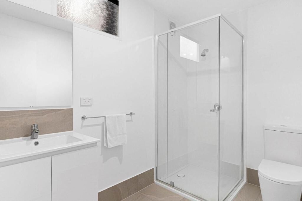 A modern bathroom with a glass shower enclosure, a white sink, and a toilet.