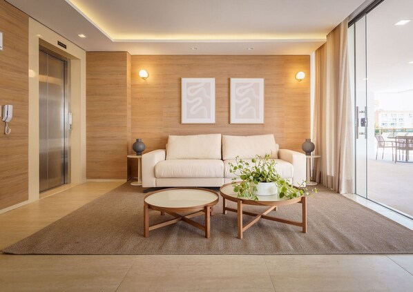 A modern living room with a beige sofa, two side tables, a coffee table, and a large window with a view of the outside.