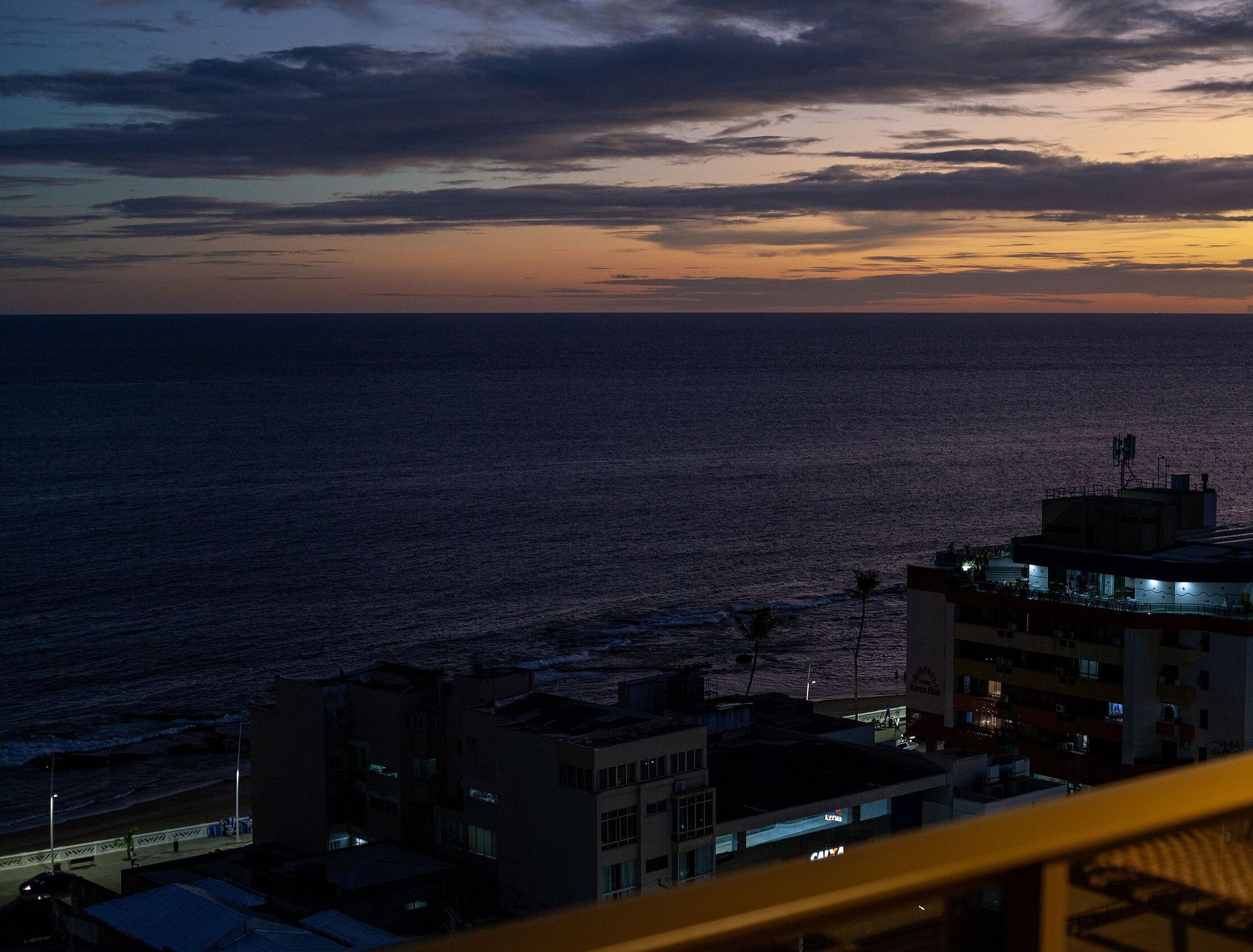 Vista costera al atardecer con edificios y una playa en primer plano.