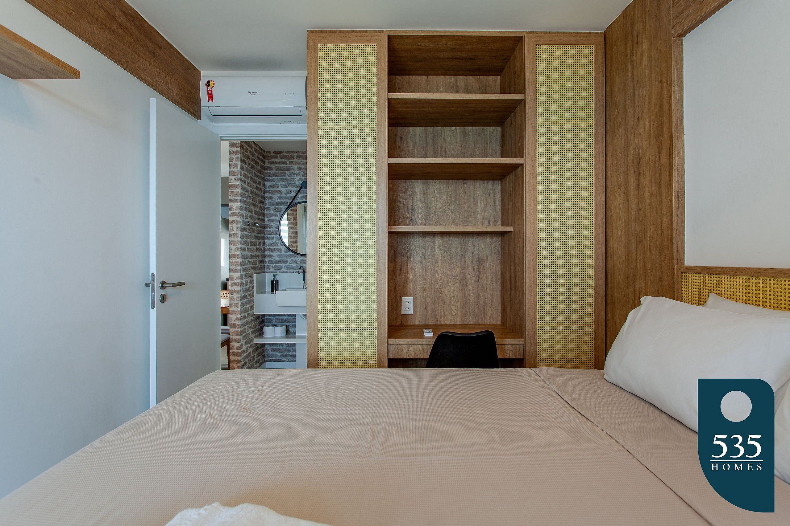 A bedroom with a bed, a wooden wardrobe, a desk, and a bathroom visible through an open door.