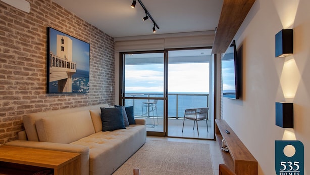 A modern living room with a brick wall, a large window, a sofa, a coffee table, and a TV mounted on the wall.