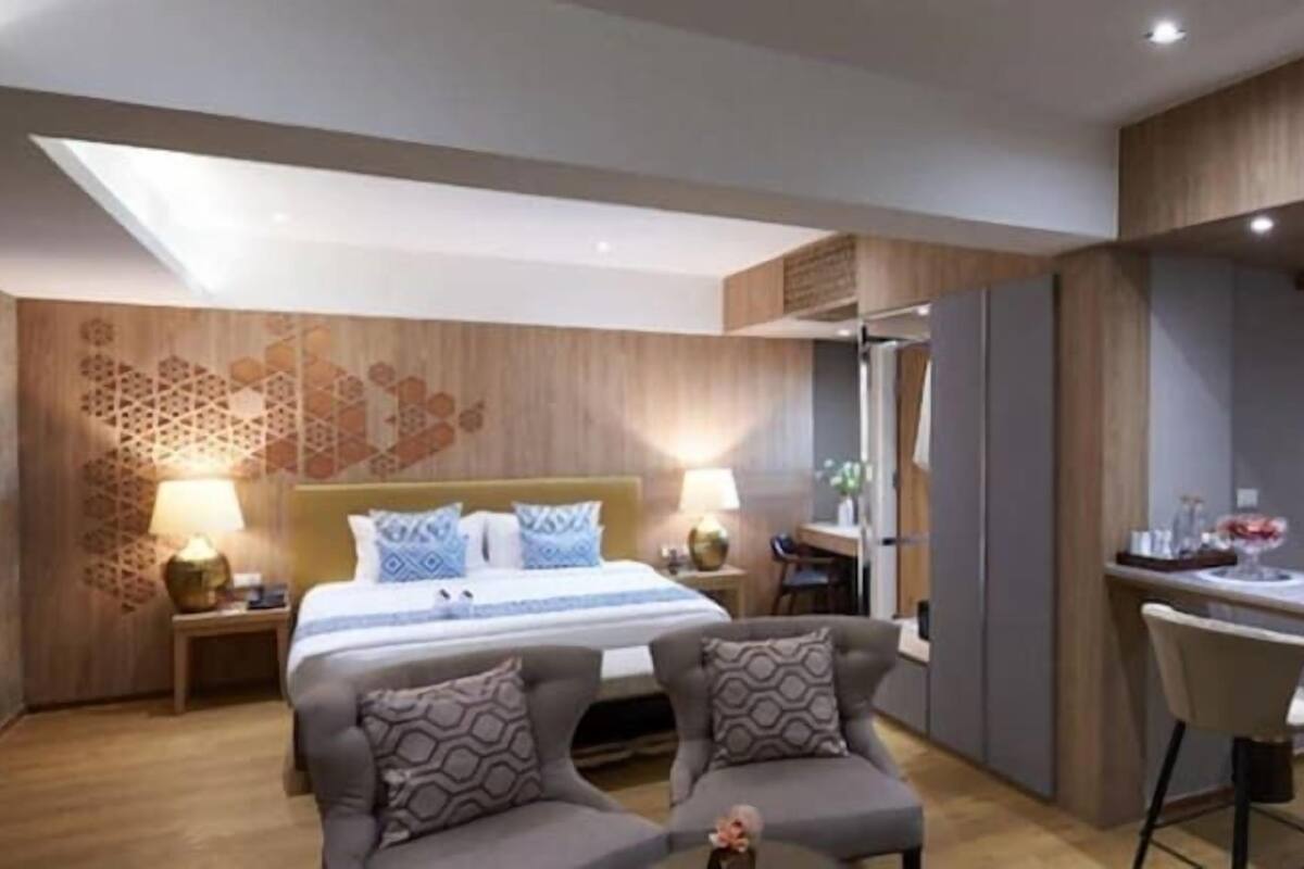 Quarto de hotel moderno com cama, duas poltronas, um pequeno espaço de refeições com micro-ondas e um painel decorativo na parede.