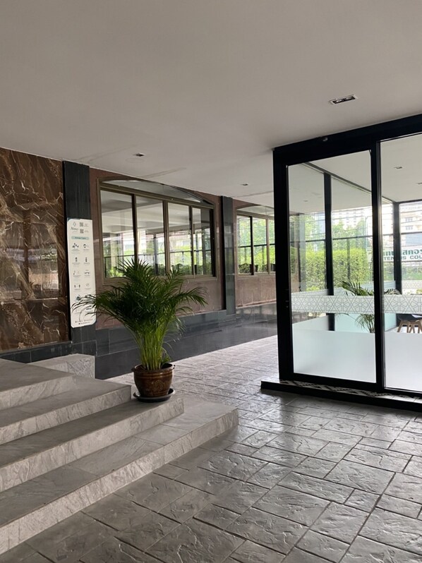 Entrada moderna de un edificio con escalones de mármol, una planta en maceta y amplias puertas de cristal que dan a un espacio exterior.