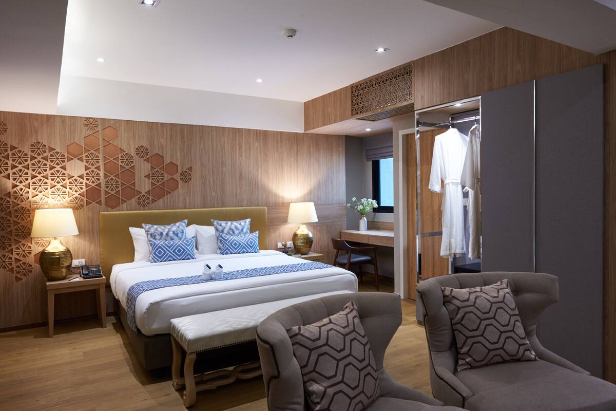 Quarto de hotel moderno com uma cama grande, mesas de cabeceira com abajures, uma escrivaninha e um guarda-roupa.