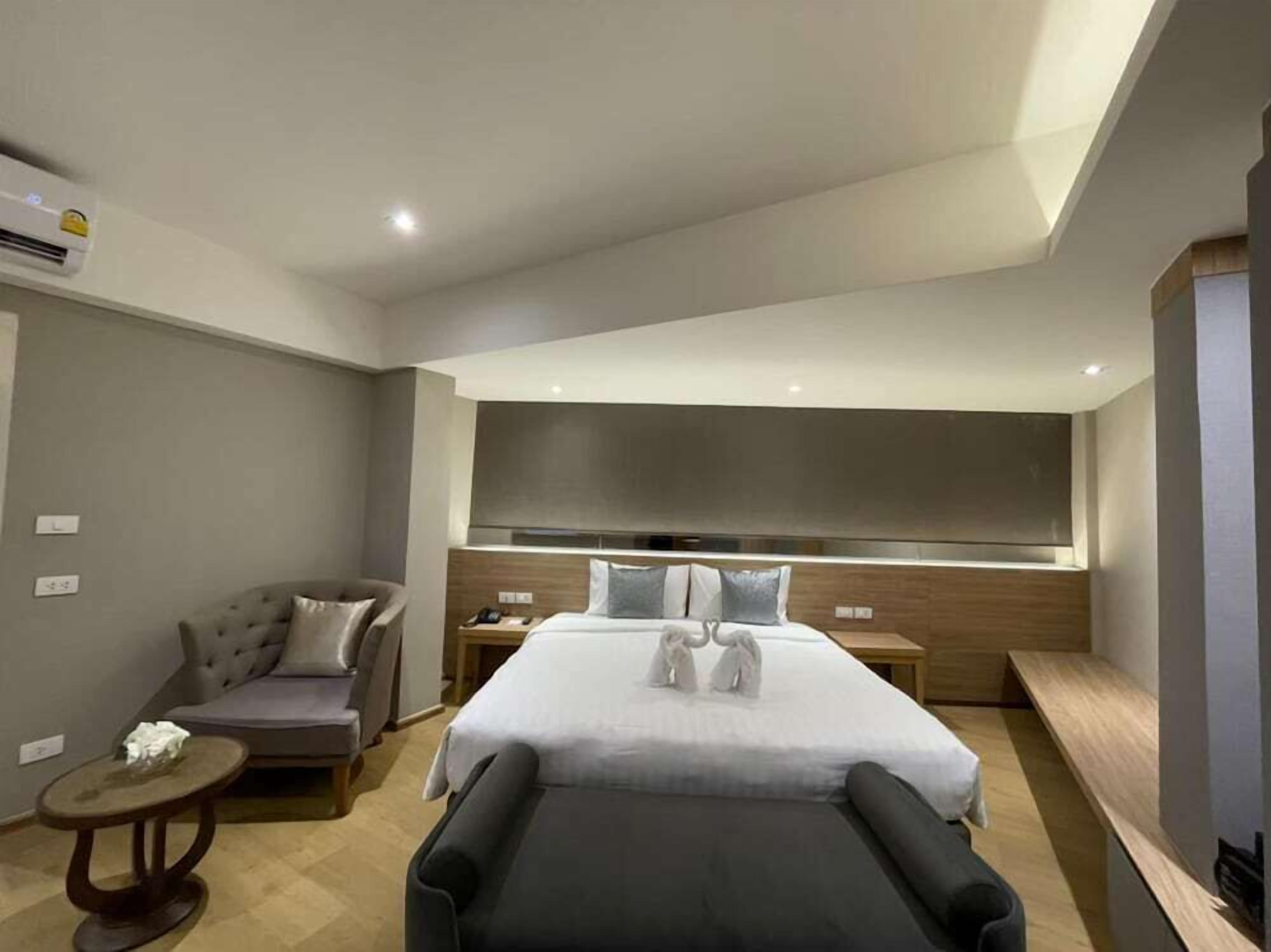 A modern hotel room with a large bed, a sofa, a small table, and a massage chair.