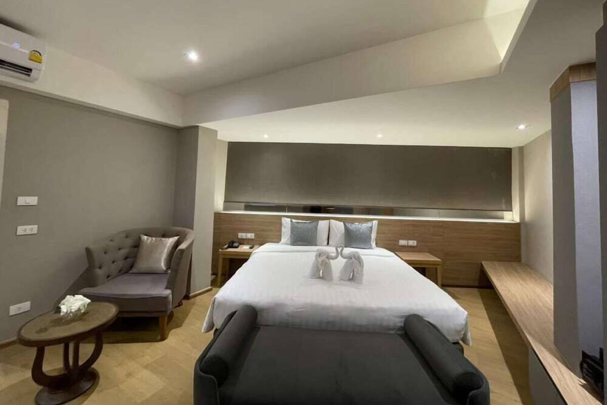 Quarto de hotel moderno com uma cama grande, um sofá, uma mesinha e uma cadeira de massagem.