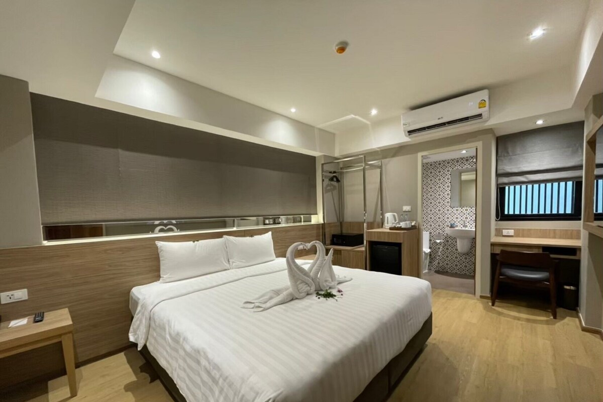 Ein modernes Hotelzimmer mit einem großen Bett, einem Schreibtisch, einer Duschkabine und einem Fernseher.
