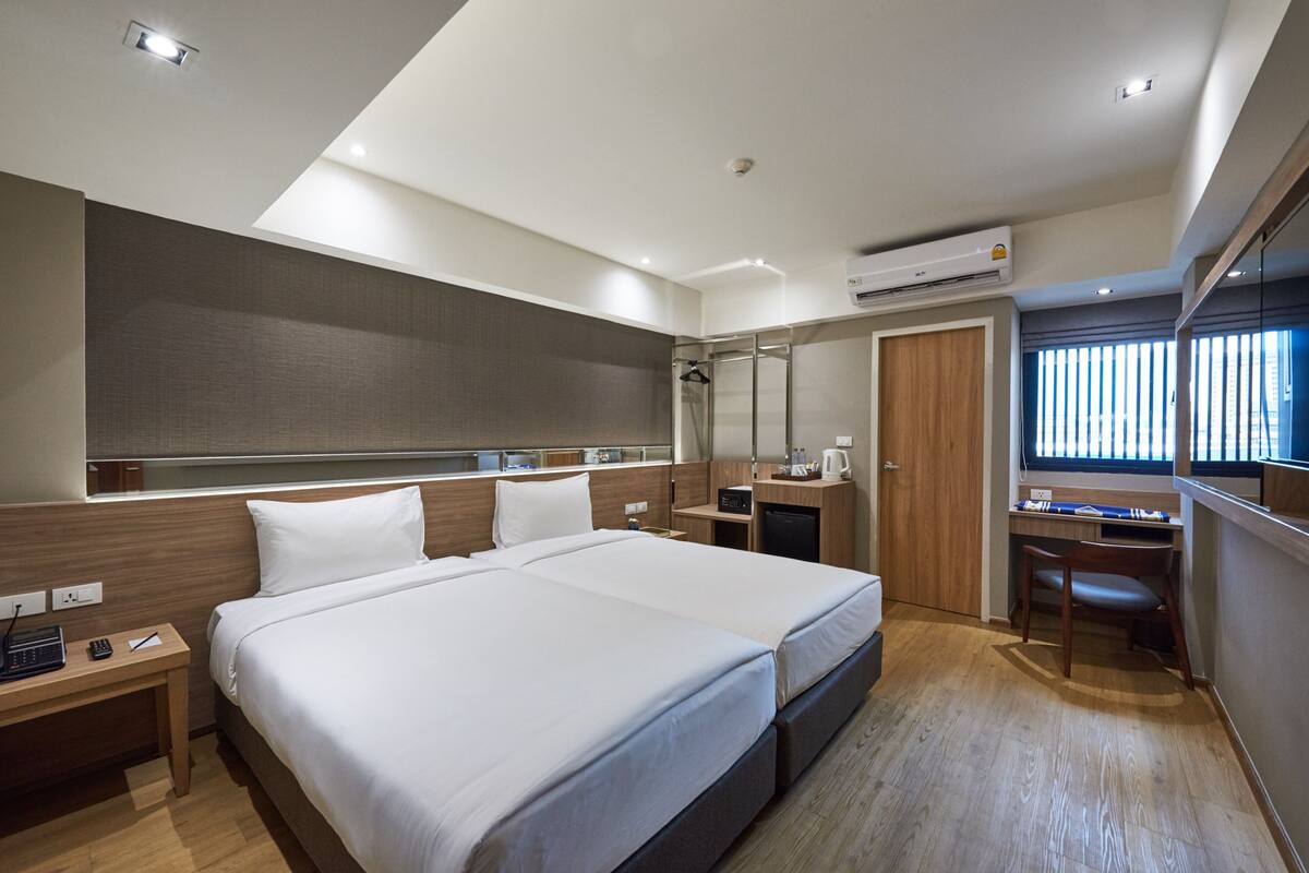 Quarto de hotel moderno com uma cama grande, uma escrivaninha e uma janela com persianas.