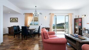 A dining area with a table and chairs, a sofa, a chandelier, and a view through a glass door. - Villa Anastasia in Corfu (Corfu)