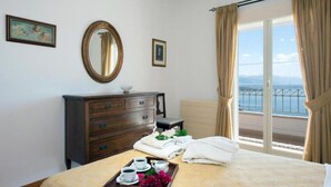 A hotel room with a bed, a dresser, a mirror, a window with curtains, and a tray with towels and cups. - Villa Anastasia in Corfu (Corfu)