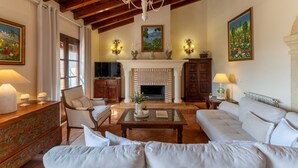 A living room with a fireplace, a sofa, a television, and decorative wall art. - Villa Mirador de Frigiliana (Frigiliana)