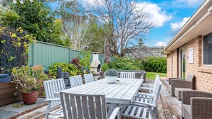 A patio with a wooden table and chairs, surrounded by potted plants and a brick wall. - Beachcomber - The Perfect Beach Getaway (Mollymook Beach)