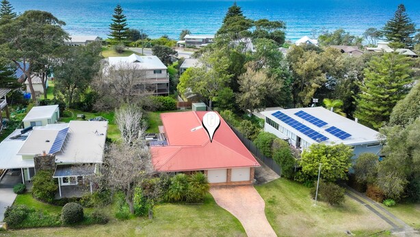 An aerial view of a residential area with houses, solar panels, and a coastal backdrop. - Beachcomber - The Perfect Beach Getaway (Mollymook Beach)