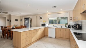 A modern kitchen with wooden cabinets, a built-in dishwasher, and a large window providing natural light. - Beachcomber - The Perfect Beach Getaway (Mollymook Beach)
