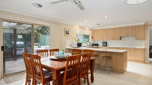 A modern kitchen with wooden cabinets, a central island, and a dining area with wooden chairs. - Beachcomber - The Perfect Beach Getaway (Mollymook Beach)