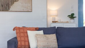 Un salon avec un canapé bleu foncé, un coussin blanc et un plaid orange.