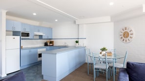 Une cuisine moderne avec des meubles bleus, un îlot central et un coin repas comprenant une table en verre et des chaises bleues.