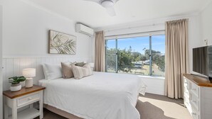 A modern bedroom with a large bed, a TV, a bedside table with a lamp, and a window with curtains.