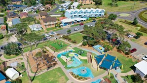 An aerial view of a residential area with a large swimming pool, playground, and a community center with a blue facade.