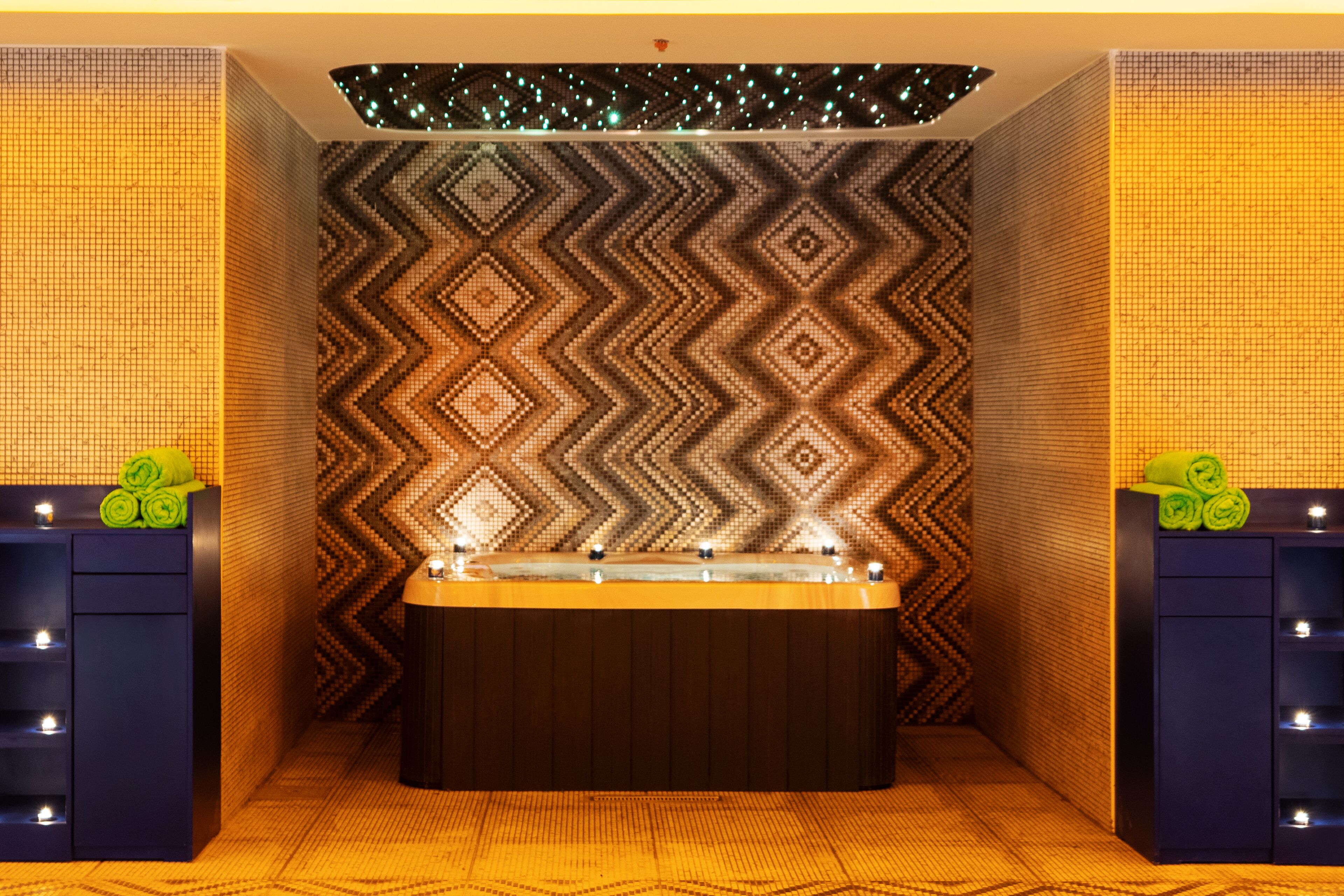 Een spa-ruimte met een patroon op de muur, een badkuip en planken met handdoeken.