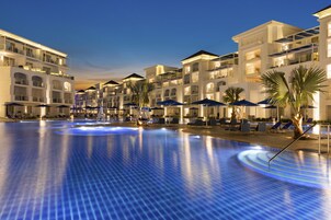 Zona de piscina de hotel con varios niveles de balcones, sillones de descanso y sombrillas.