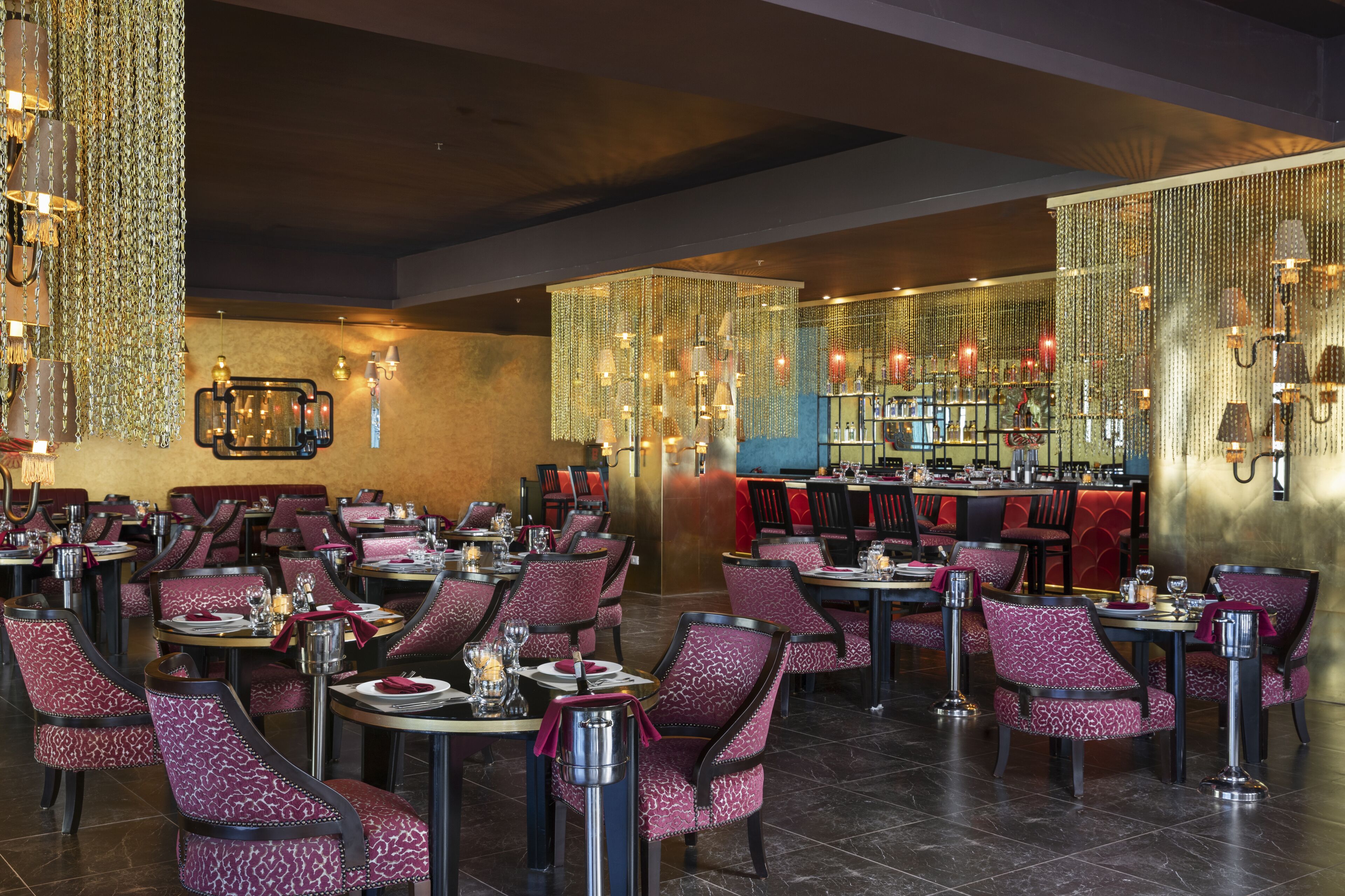 A restaurant with multiple dining tables and chairs, a bar area, and decorative hanging lights.
