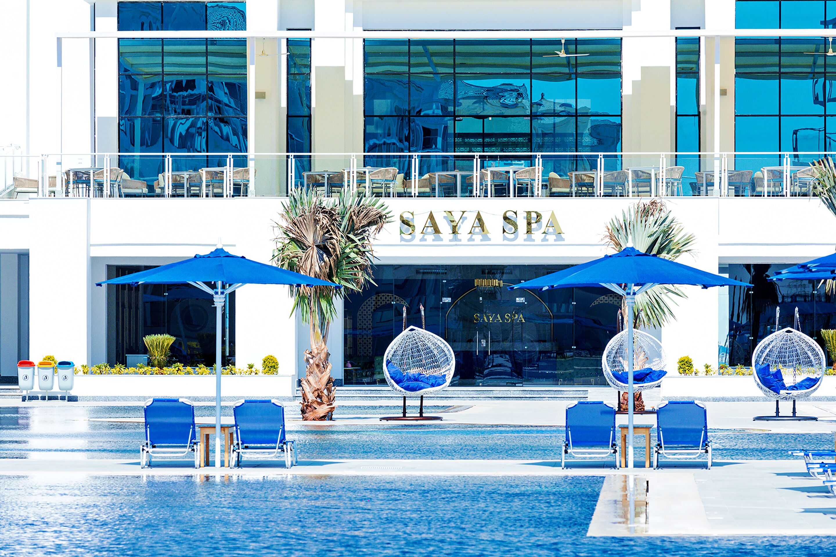 A modern hotel with a pool area featuring blue umbrellas and lounge chairs.