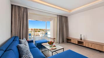 Una sala de estar moderna con un sofá azul, una mesa de centro de vidrio con fruta y vistas a una piscina y asientos al aire libre.