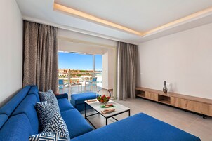 Una sala de estar moderna con un sofá azul, una mesa de centro de vidrio con fruta y vistas a una piscina y asientos al aire libre.
