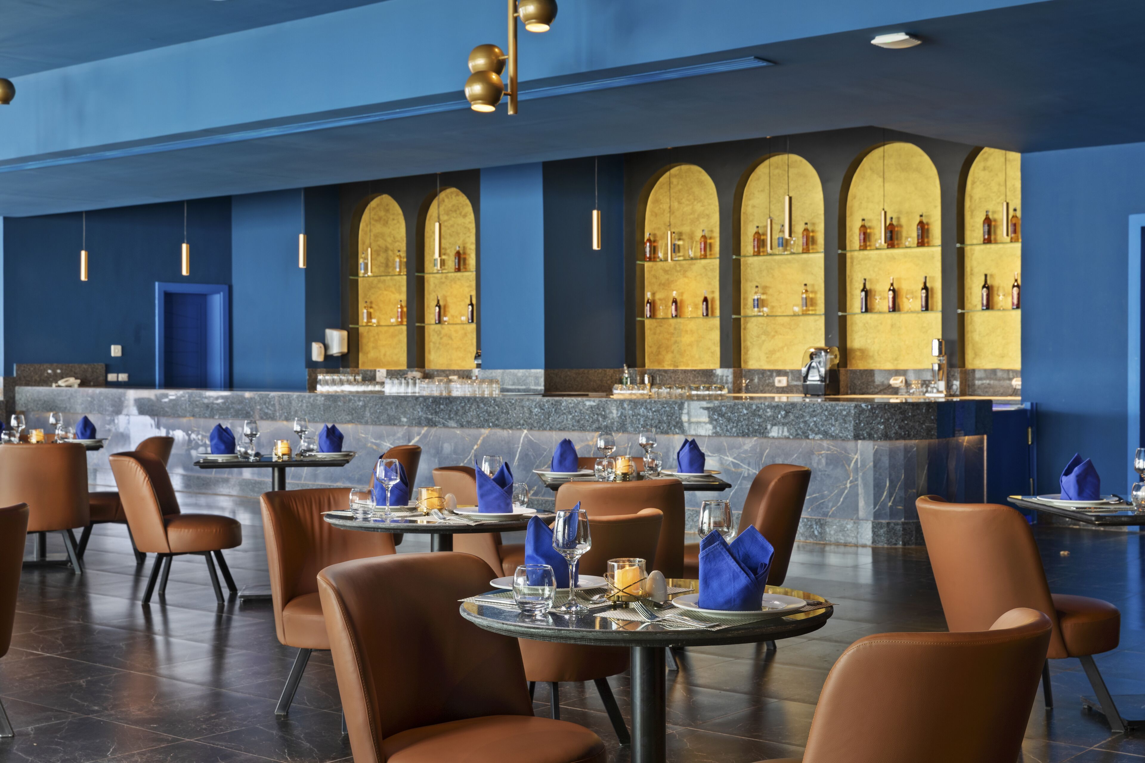 A modern restaurant with round tables, brown leather chairs, and blue napkins.