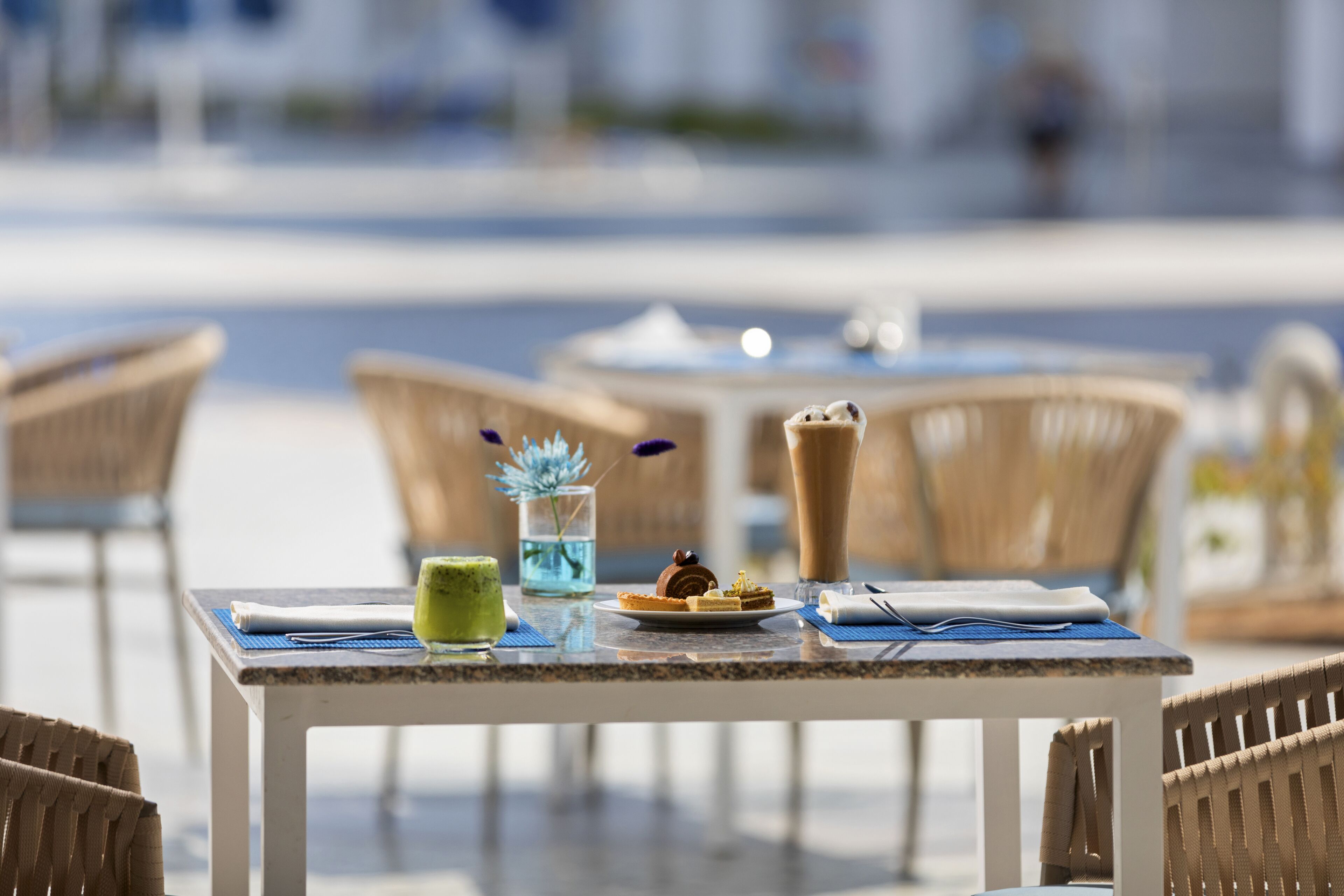 A table with a dessert, a drink, and a small vase with flowers.