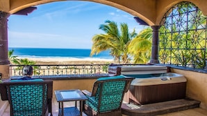 Un balcón con sillas de mimbre y una mesa, con vista a una playa y el océano.