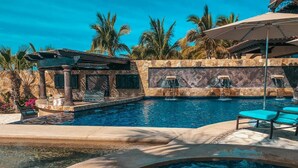 Piscina con jacuzzi, sillas de descanso y una cascada.