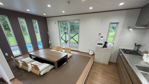 A modern kitchen with a dining area, large windows, and a view of greenery.