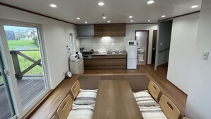 A compact kitchen with wooden cabinets, a microwave, and a refrigerator. There is a dining table with chairs in the center.