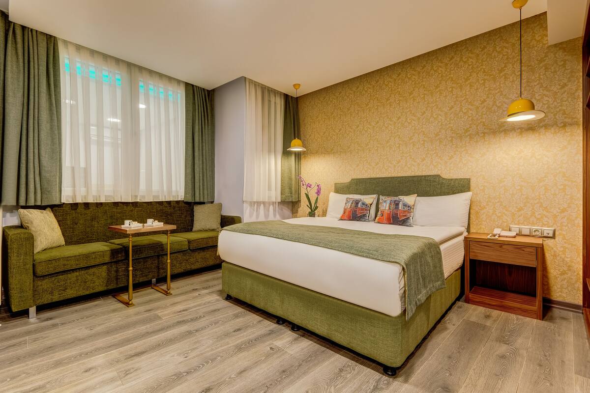 Une chambre d’hôtel avec un lit, un canapé vert, une petite table et une table de chevet avec une lampe.